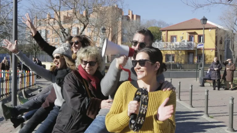 Seguimos en la manifestación y en este momento se ha generado una conga entre los padres y madres de los niños/as. Una toca la pandereta, un padre sujeta un megáfona y el resto cantan y bailan. Al fondo, dos señoras miran y miran la escena inquietas.